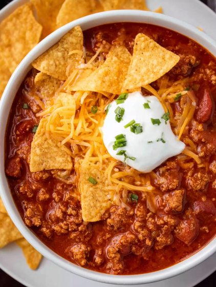 A bowl of chili with a dollop of sour cream and a sprinkle of chips.
