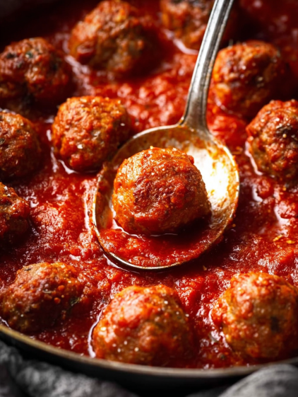 A spoon in a bowl of meatballs.