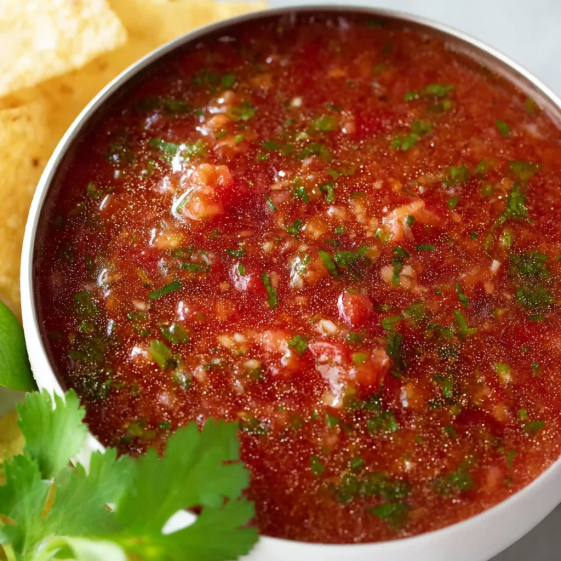 A bowl of salsa with chips on the side.