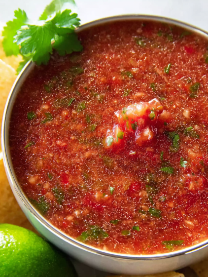 A bowl of salsa with green toppings.