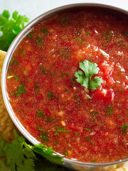A bowl of red sauce with a green herb on top.