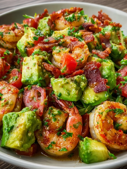 A close up of a salad with shrimp, avocado, and bacon.