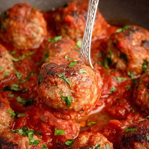 A fork is stuck in a plate of meatballs.